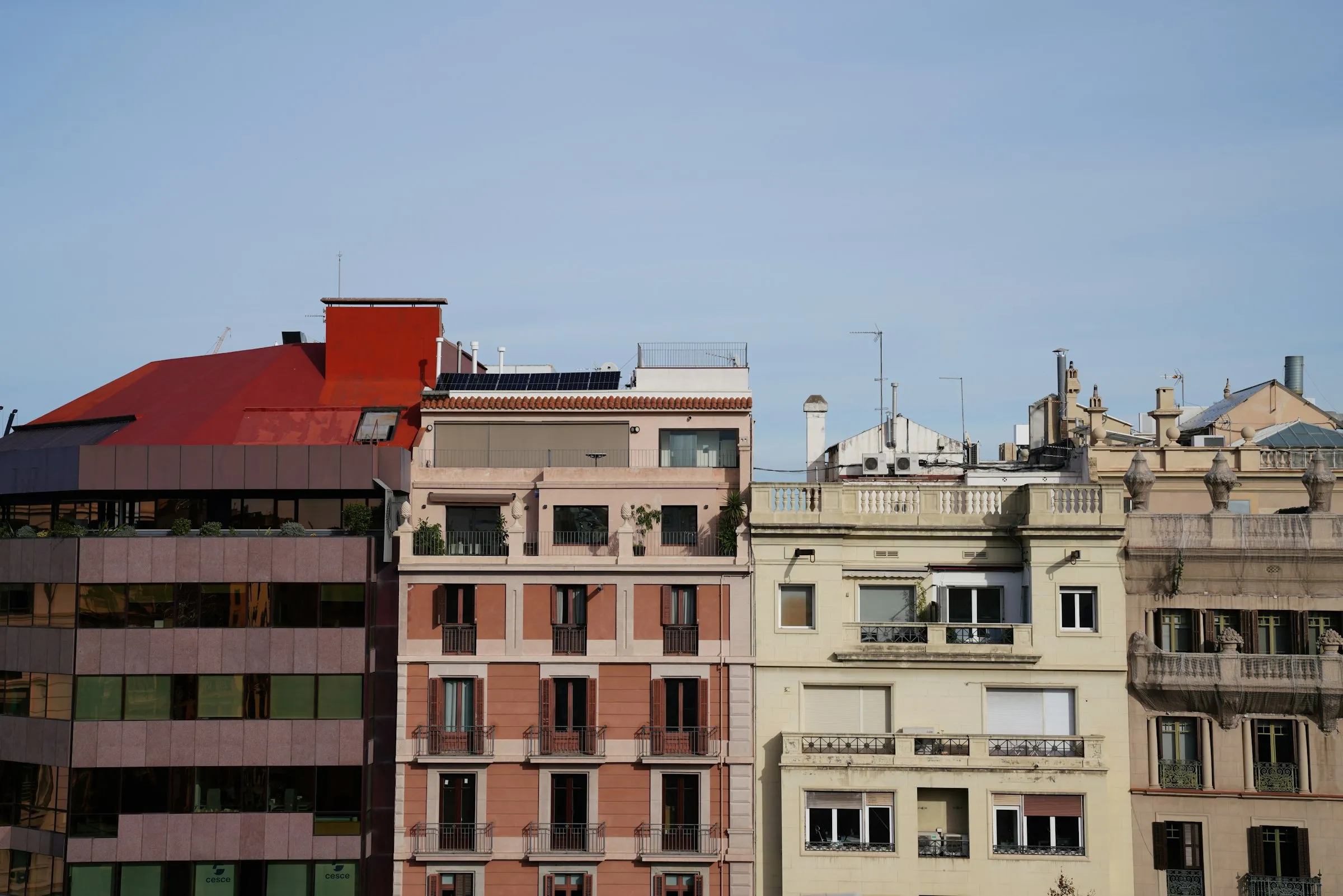 Fila de edificios residenciales coloridos en Barcelona bajo cielo despejado, con fachadas de distintos estilos arquitectónicos y balcones